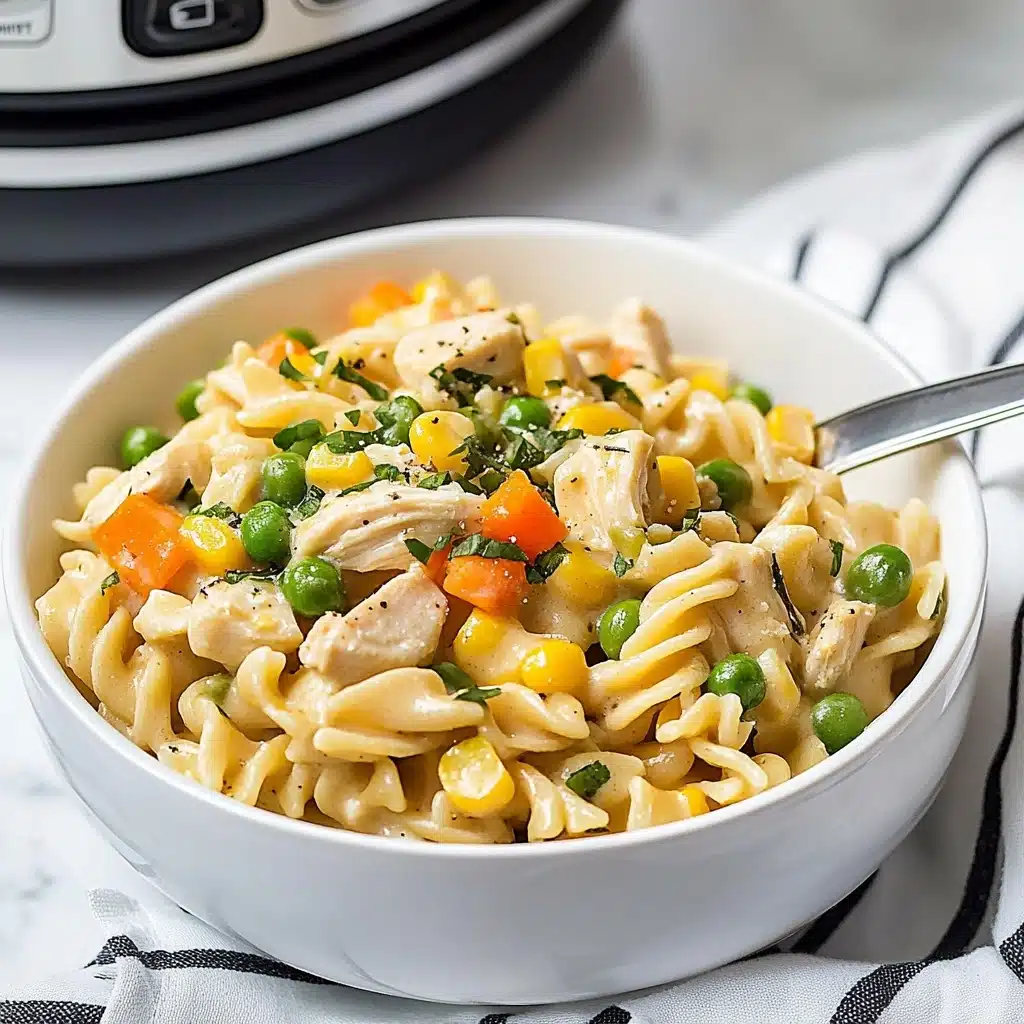 Instant Pot Cheesy Chicken, Noodles, and Vegetables, cheesy chicken pasta recipe, quick one-pot chicken dinner, hearty Instant Pot chicken dish, easy cheesy chicken and noodle recipe A white bowl filled with creamy pasta that has three visible layers: the bottom layer is light yellow twisted noodles, the middle layer has small chunks of white chicken meat, and the top layer is mixed vegetables including green beans, corn, peas, and small orange carrot cubes, all sprinkled with chopped green herbs and black pepper. There is a silver spoon placed inside the bowl on the right side, and the bowl sits on a white marbled surface with a white cloth with black stripes beside it. In the background, a grey and black instant pot is slightly visible.