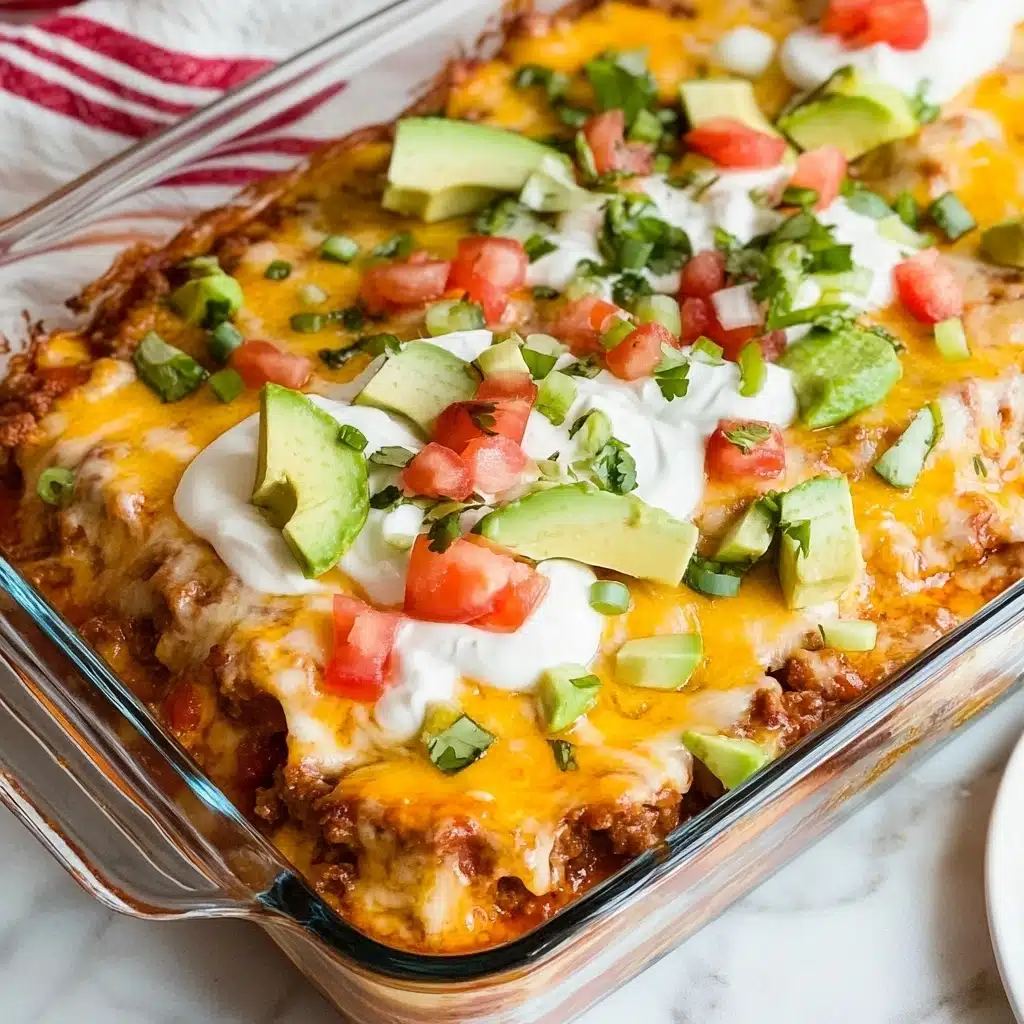 Ground Beef Enchiladas, easy enchilada recipe, cheesy beef enchiladas, quick Mexican dinner, beginner-friendly enchiladas A clear glass square baking dish filled with a layered casserole sits on a white marbled surface. The bottom layer is made of a rich, reddish sauce with visible bits of ground meat. On top, a thick layer of melted yellow and white cheese covers the casserole, melted evenly with some brown spots. The next layer includes a generous row of dollops of light sour cream along the middle. Fresh diced red tomatoes and pale green avocado slices are scattered on the sour cream. Bright green chopped scallions are sprinkled over the top and around the edges. A white cloth with red stripes is partially visible in the top left corner, and a white plate is placed on the bottom right.