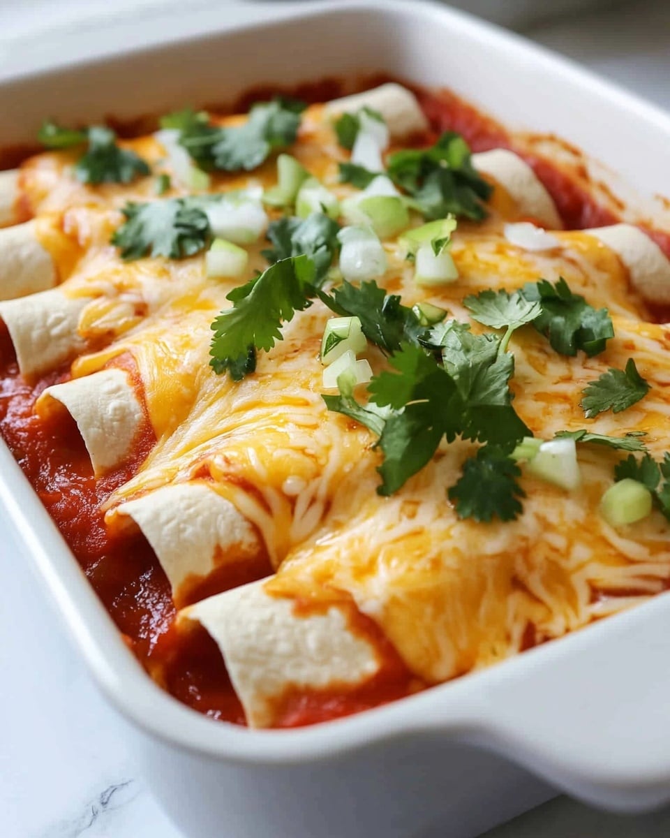 A white baking dish holds six rolled tortillas lined up in one layer, each tortilla pale yellow with a soft texture. They are covered with a bright red tomato sauce that pools slightly around the edges of the tortillas. On top of the sauce is a layer of melted shredded cheese, showing a blend of golden yellow and white colors with a smooth melted texture. Fresh green cilantro leaves are scattered evenly over the cheese for a pop of color. The dish sits on a white marbled surface, with some blurred white tile background in soft focus. Photo taken with an iphone --ar 4:5 --v 6.1