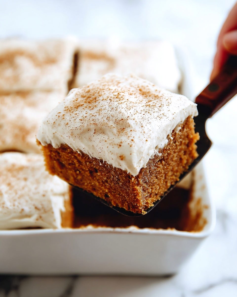 A close-up view shows a square piece of moist, brown cake with a thick layer of smooth, creamy white frosting on top, sprinkled lightly with cinnamon or a similar spice. The cake layer is dense and textured, while the frosting looks soft and slightly glossy. The square piece is lifted out from a white baking dish, revealing more pieces of the same frosted cake inside. A woman's hand is holding a dark wooden-handled utensil to lift the piece. The background surface has a white marbled texture. photo taken with an iphone --ar 4:5 --v 7