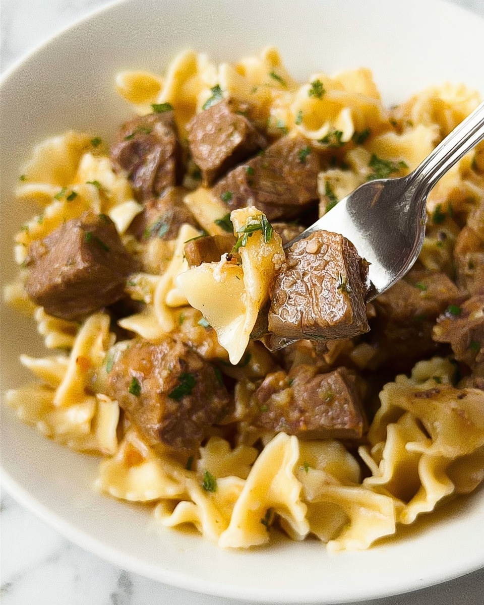 The image shows a close-up of a white plate filled with a dish made of pasta and chunks of brown cooked meat. The pasta is a pale yellow with ruffled edges and a soft texture, layered underneath and mixed with the meat pieces. The brown meat cubes have a slightly moist and tender look, coated with a light sauce that has a few visible herbs sprinkled on top. There is a silver fork in the dish, holding a piece of meat and some pasta, ready to be eaten. The plate is set on a white marbled surface. photo taken with an iphone --ar 4:5 --v 7