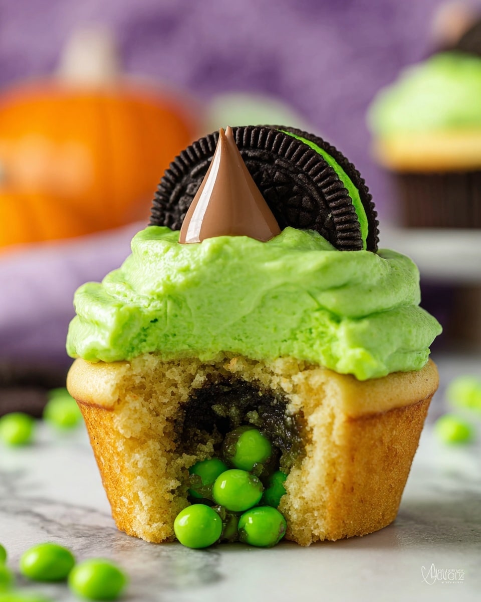 A close-up of a vanilla cupcake with bright green frosting spread thickly on top, slightly melting over the edges. The cupcake is opened in the front, revealing small green candy balls spilling out from inside. On top of the green frosting, there is a dark chocolate sandwich cookie placed flat with its cream side down, and sitting on the cookie is a milk chocolate drop with a pointed tip. The cupcake sits on a white marbled surface, with soft background elements blurred out but showing hints of orange and purple colors. photo taken with an iphone --ar 4:5 --v 7