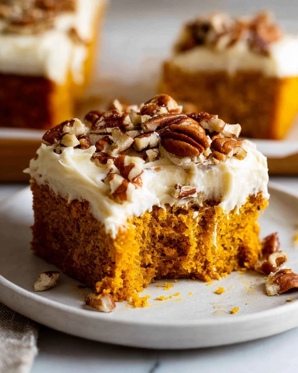 The image shows a close-up of a square slice of pumpkin cake with one bite taken out of it. The cake has two main layers: the bottom layer is a moist, bright orange pumpkin cake with a soft and slightly crumbly texture, while the top layer is a thick, creamy white frosting. The frosting is topped with chopped pecans, some whole and some broken, adding a brown, crunchy texture on top. The piece of cake sits on a white plate placed on a white marbled surface, with another similar cake slice blurred in the background. Photo taken with an iphone --ar 4:5 --v 7