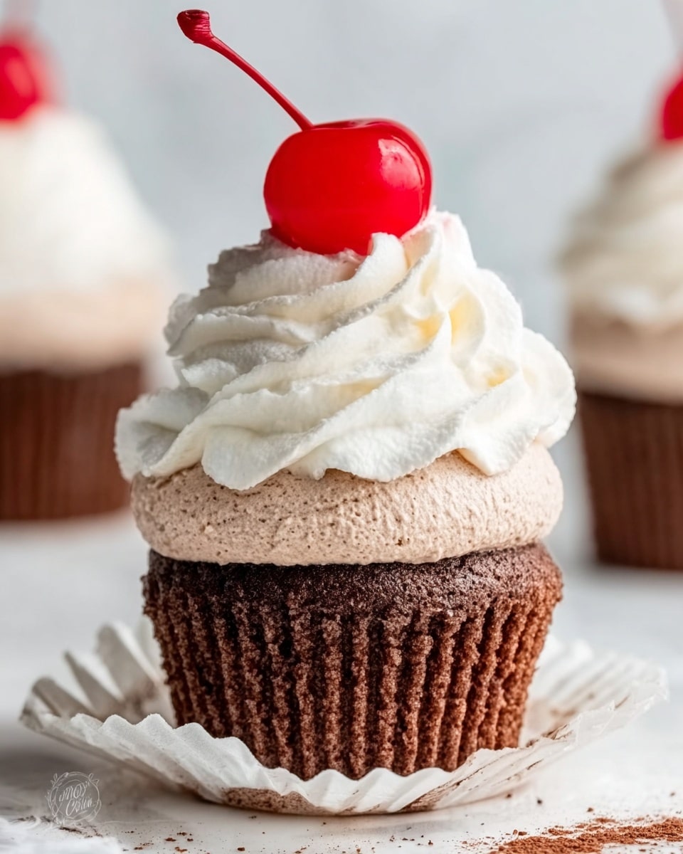 The image shows a close-up of a chocolate cupcake with three layers. The bottom layer is a dark brown chocolate cake with a soft and moist texture. On top of this is a thick layer of light brown chocolate frosting that looks creamy and smooth. Above the frosting is a thick white swirl of whipped cream, soft and fluffy. On the very top of the cupcake sits a bright red cherry with a long stem. The cupcake liner is white and partially peeled back, resting on a white marbled surface with some crumbs scattered around. The photo taken with an iphone --ar 4:5 --v 7