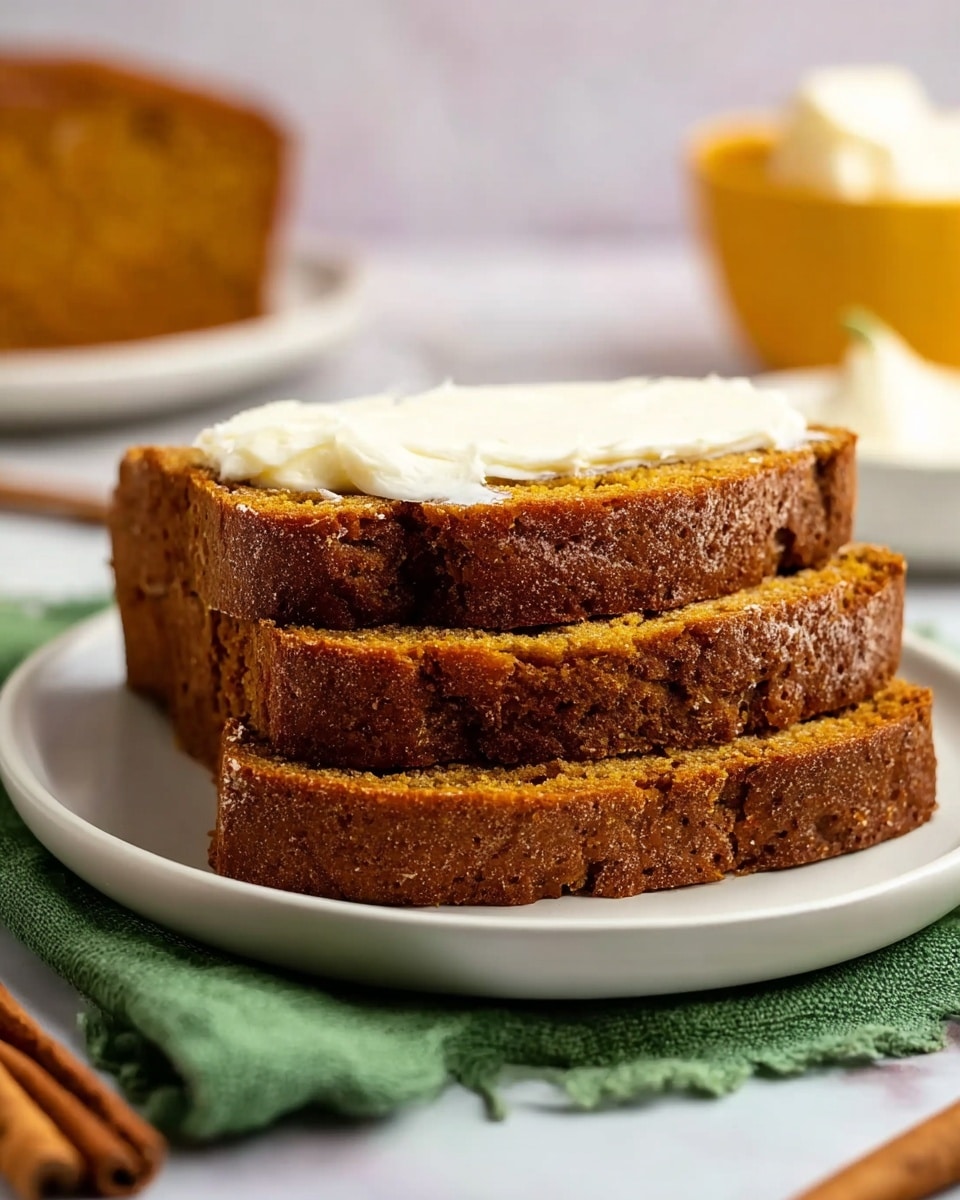 A white plate holds a single slice of brown pumpkin bread spread with a creamy light yellow layer of butter. Next to it on the white marbled surface are three more slices of pumpkin bread, arranged with one slice topped with butter overlapping the other two plain slices. At the top right corner, part of the pumpkin bread loaf is visible, resting on parchment paper. To the top left, a small beige bowl with several squares of butter sits beside three cinnamon sticks, while two silver forks lie near the left edge. A folded green cloth with a diagonal line pattern is spread under the parchment and the butter bowl. At the bottom right, the bright orange rounded shape of a pumpkin appears. Photo taken with an iphone --ar 4:5 --v 7