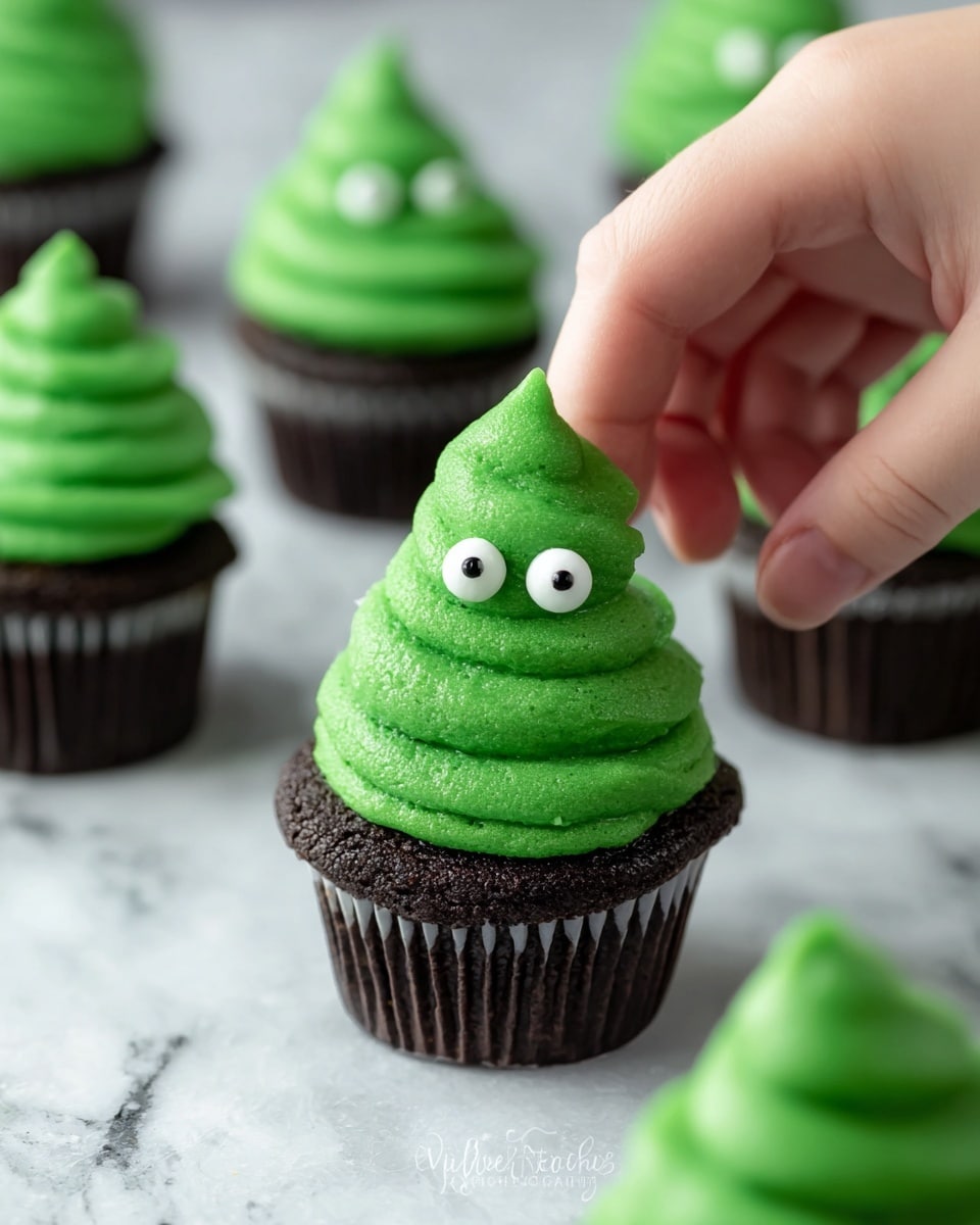 A dark green cupcake sits at the bottom layer, topped with a thick swirl of bright green frosting shaped like a small peak with ridges. Two round white candy eyes with black centers are placed near the top of the frosting, giving it a playful look. A woman's hand is gently holding this cupcake from the top. Surrounding it are other similar cupcakes on a white marbled textured surface. The overall colors are green, black, and white, with a soft, smooth texture on the frosting. Photo taken with an iphone --ar 4:5 --v 7