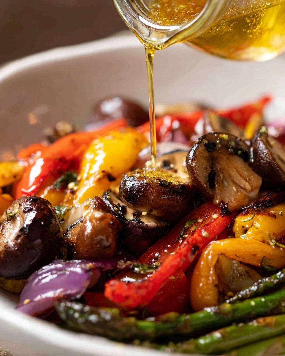 The dish shows a white bowl filled with roasted vegetables in close-up. The vegetables include whole brown mushrooms placed on top at the center, bright red and yellow roasted peppers scattered throughout the bowl, charred purple onion slices, and dark green asparagus partially visible at the bottom edge. A golden liquid, likely oil or dressing, is poured from a tilted clear jar over the mushrooms, adding a shiny glaze to the vegetables. The background is softly blurred, highlighting the colorful textures and slight charring on the veggies. The photo taken with an iphone --ar 4:5 --v 7